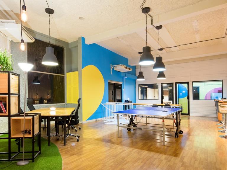 Aufnahme eines Startup-Büros. Mitten im Raum steht eine Tischtennisplatte. An der Seite Sitzgelegenheiten und eine Bar.