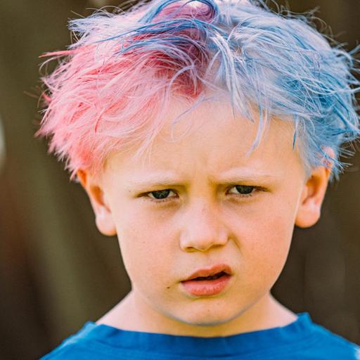 Ein Kind mit zusammengeschobenen Augenbrauen und hochgezogenem Mundwinkel. Die Haare sind zur Hälfte pink und zur Hälfte blau.