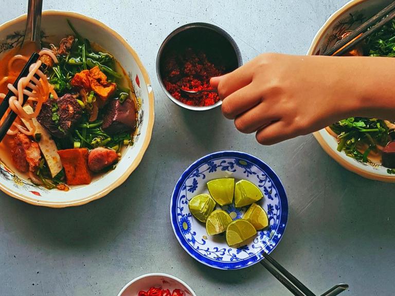 Draufsicht auf verschiedene Schalen mit asiatischem Essen, dazu eine Hand die nach Essen greift.
