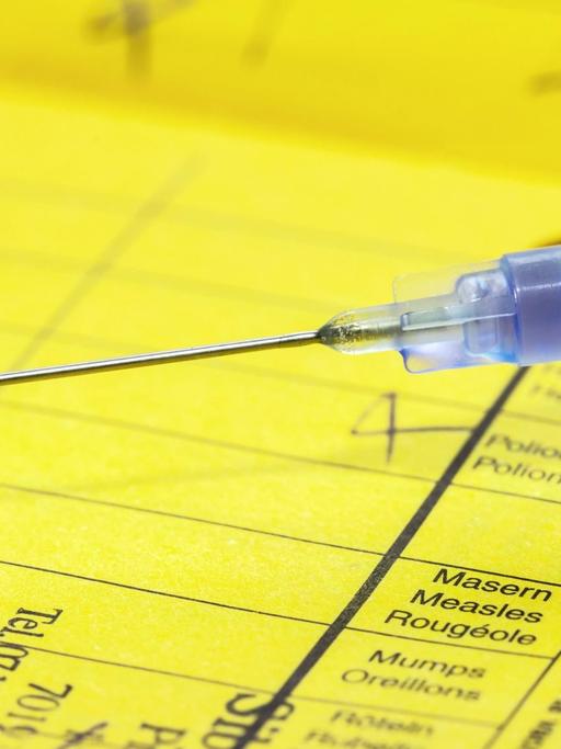 Ein gelber Impfpass mit einer Spritze mit dem Impfpfstoff gegen Masern in Nahaufnahme.