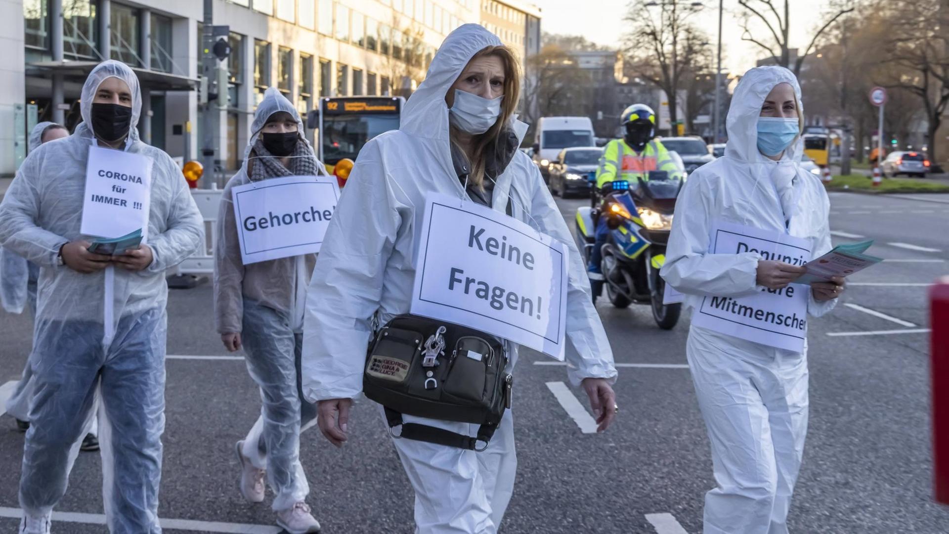 Demonstranten in Schutzanzüge tragen Plakate mit Aufschriften wie "Keine Fragen!" oder "Gehorche!" um den Hals. Demonstranten in Schutzanzüge tragen Plakate mit Aufschriften wie "Keine Fragen!" oder "Gehorche!" um den Hals.
