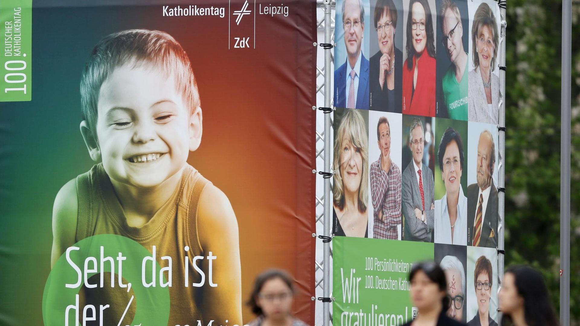 Passanten laufen an einer viereckigen Installation mit Transparenten vorbei. Auf der Vorserseite sieht man das überlebensgroße Bild eines grinsenden Jungen und die Schrift "Seht, da ist der Mensch". Passanten laufen an einer viereckigen Installation mit Transparenten vorbei. Auf der Vorserseite sieht man das überlebensgroße Bild eines grinsenden Jungen und die Schrift "Seht, da ist der Mensch".