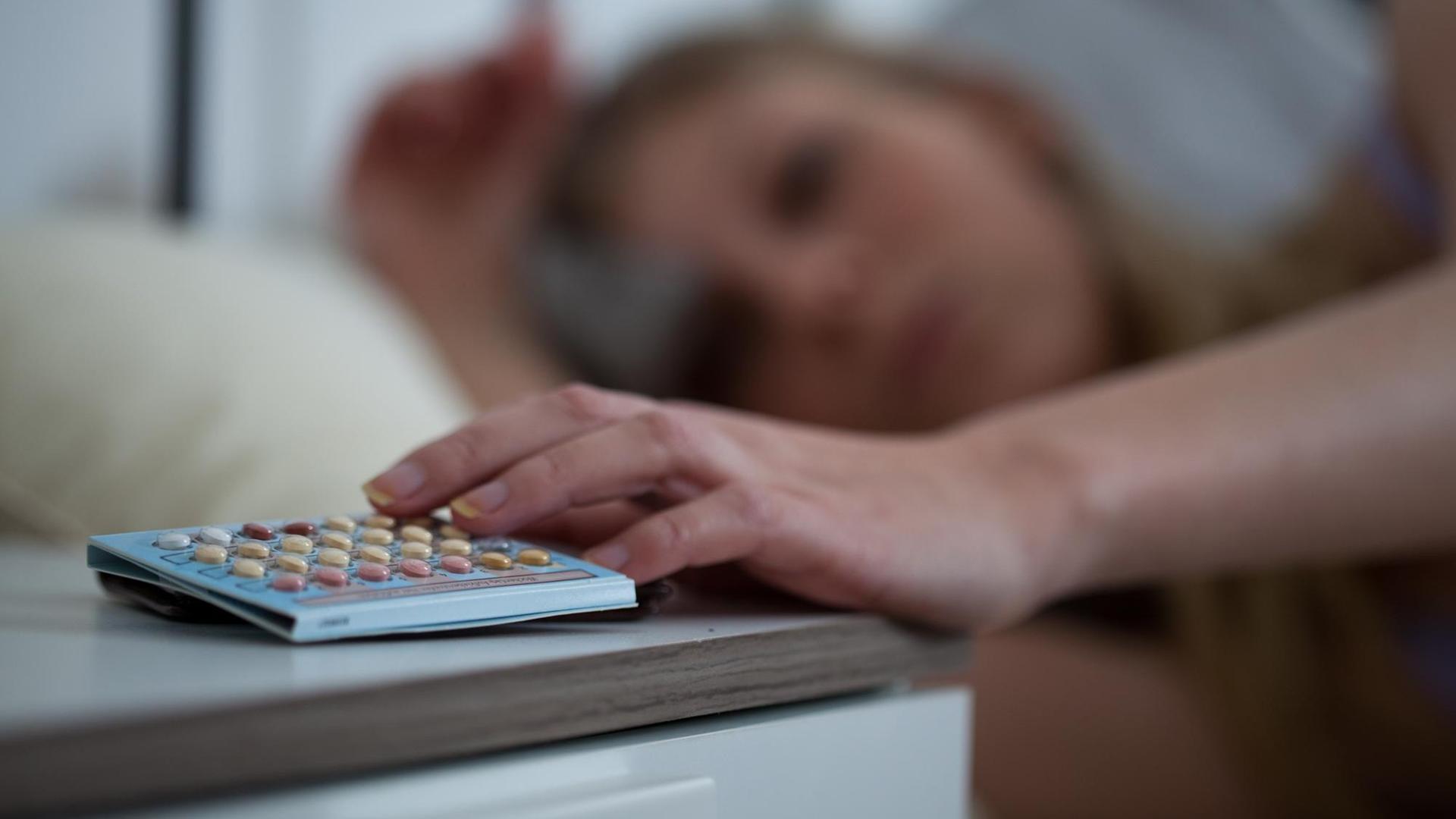 Eine Frau greift am nach ihrer Pille, die auf dem Nachtschrank liegt Eine Frau greift am nach ihrer Pille, die auf dem Nachtschrank liegt