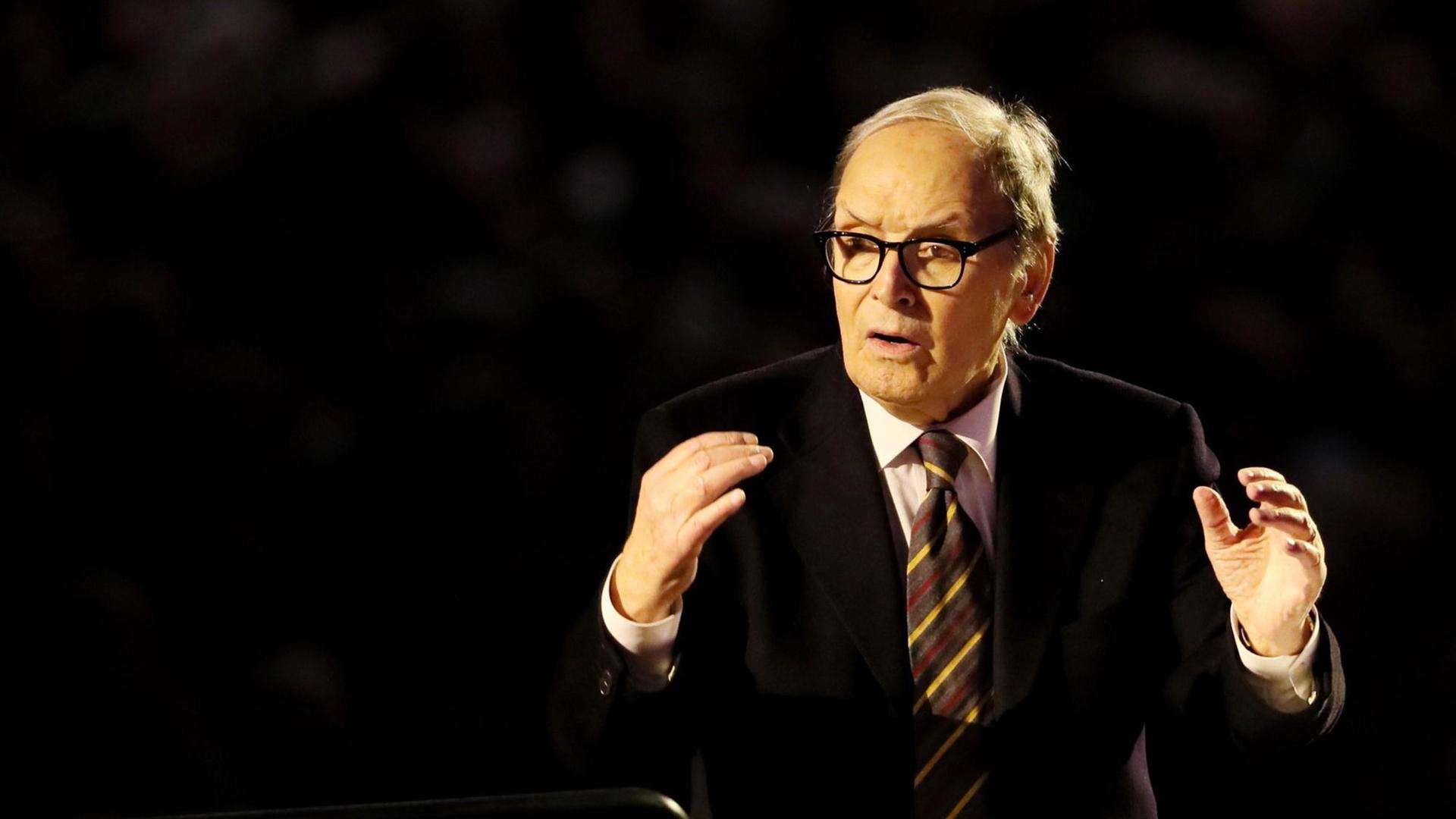 Ennio Morricone in weißem Hemd, dunklem Jackett und Krawatte beim Dirigieren. Ennio Morricone in weißem Hemd, dunklem Jackett und Krawatte beim Dirigieren.