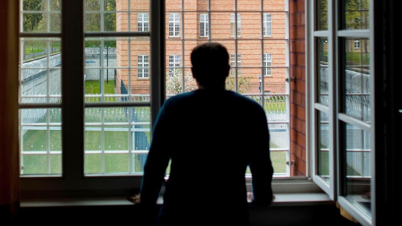 Die Silhouette eines Mannes vor einem vergitterten Fenster.