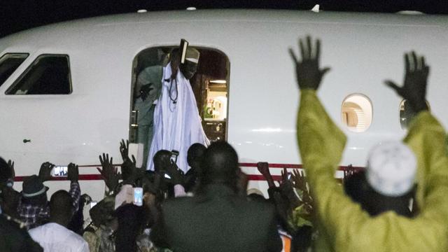 Es ist Nacht. Jammeh winkt vom EInstieg aus seinen ihn feiernden Anhängern zu, die man im Vordergrund sieht.