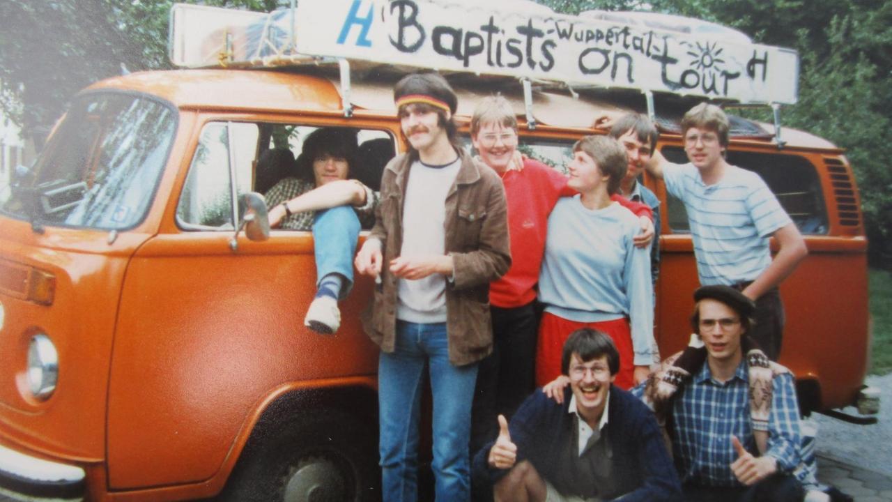 Ein oranger VW-Bus mit einer Gruppe junger Leute und der Aufschrift "Baptists on tour" auf einem Foto von 1984