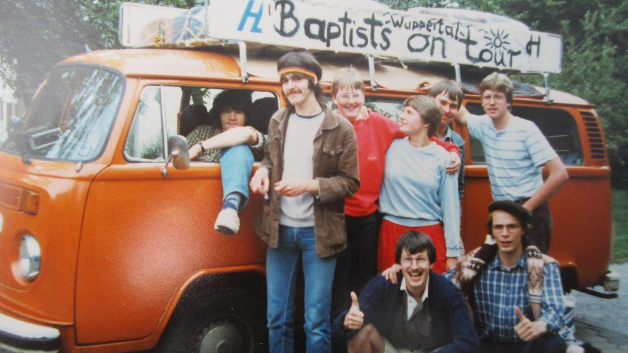 Ein oranger VW-Bus mit einer Gruppe junger Leute und der Aufschrift "Baptists on tour" auf einem Foto von 1984 Ein oranger VW-Bus mit einer Gruppe junger Leute und der Aufschrift "Baptists on tour" auf einem Foto von 1984