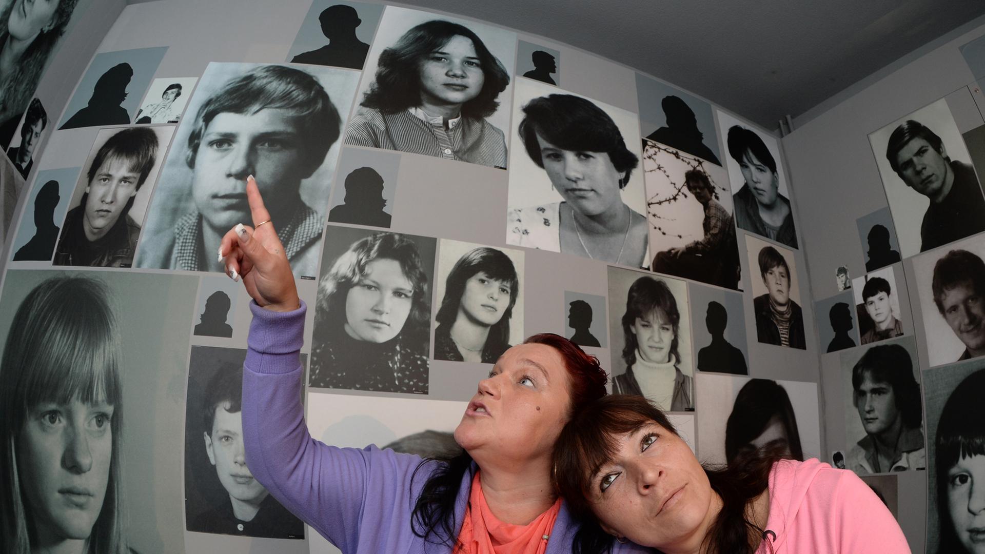 In einem Raum mit Porträtfotos sitzen Jana Mendes Bogas (l) und Ilona Dothe am 14.09.2013 auf einem Treffen ehemaliger DDR-Heimkinder in der "Gedenkstätte Geschlossener Jugendwerkhof" in Torgau (Sachsen).