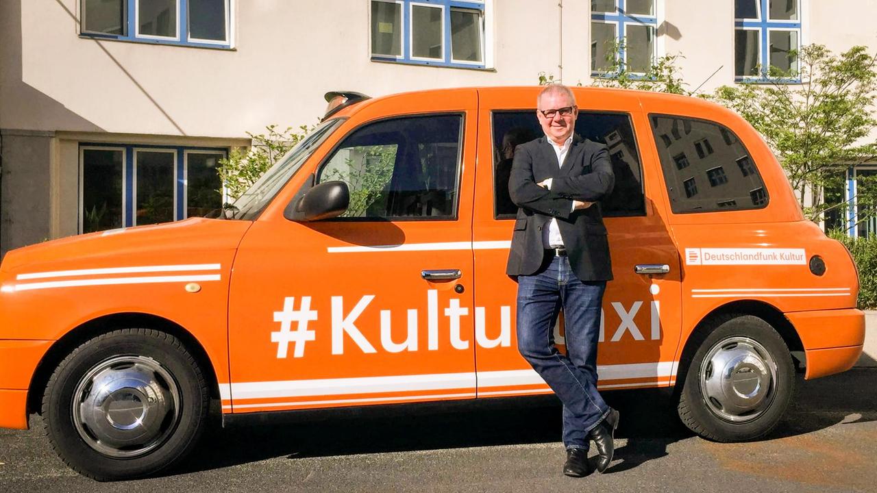 Der Schauspieler Joachim Krol steht in freudiger Erwartung auf die Sendung "Im Gespräch" vor dem orange lackierten Kulturtaxi des Deutschlandfunks am Hans Rosenthal Platz. Der Schauspieler Joachim Krol steht in freudiger Erwartung auf die Sendung "Im Gespräch" vor dem orange lackierten Kulturtaxi des Deutschlandfunks am Hans Rosenthal Platz.