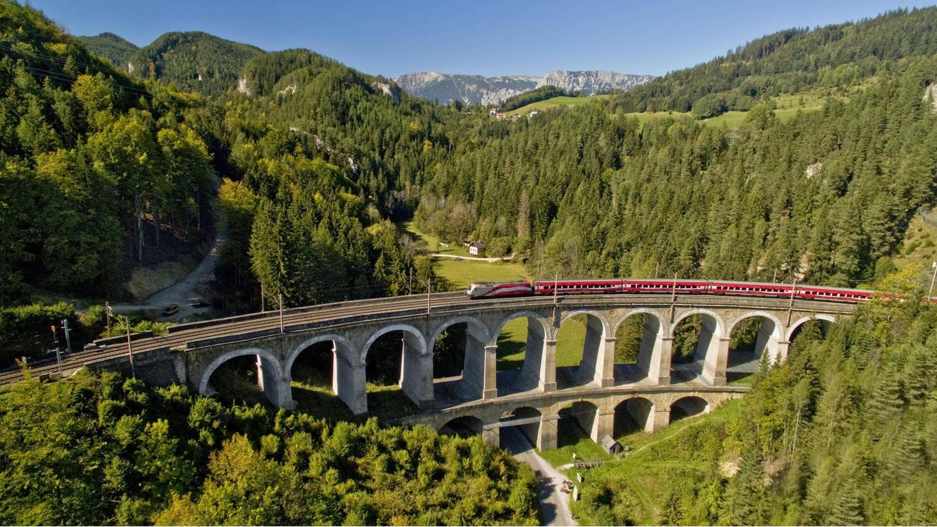 Zwischen Wäldern und Bergen fährt auf einem Viadukt ein Zug Zwischen Wäldern und Bergen fährt auf einem Viadukt ein Zug