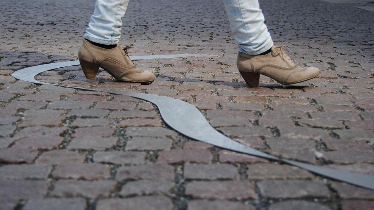 Füße laufen über ein metallenes Band, das im Pflaster eingelassen ist. Füße laufen über ein metallenes Band, das im Pflaster eingelassen ist.