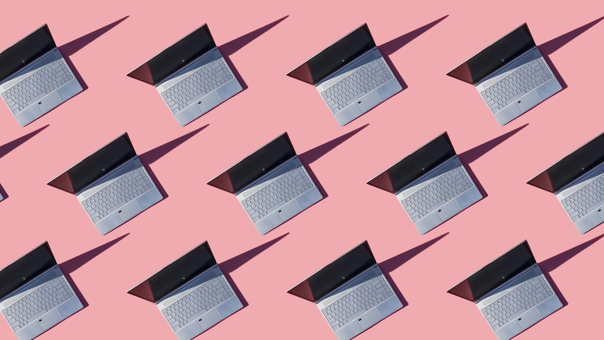 Zahlreiche Laptops stehen aufgeklappt auf pinkem Untergrund. Zahlreiche Laptops stehen aufgeklappt auf pinkem Untergrund.