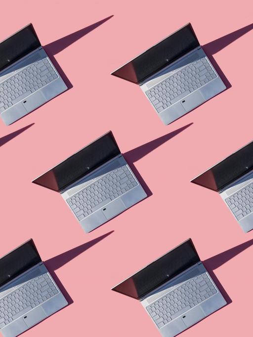 Zahlreiche Laptops stehen aufgeklappt auf pinkem Untergrund.