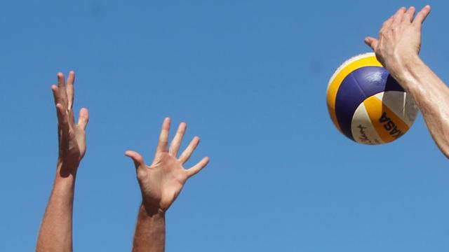 Ein Spieler schlägt, ein anderer blockt einen Volleyball