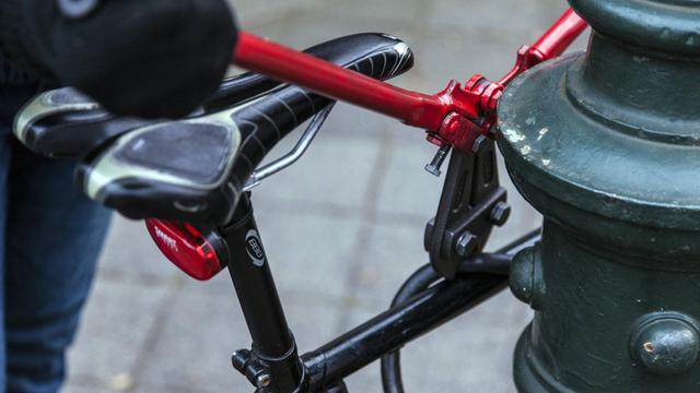 Fahrraddiebstahl: Ein Bolzenschneider knackt ein Fahradschloss von einem Rad, dass an einer Laterne steht.