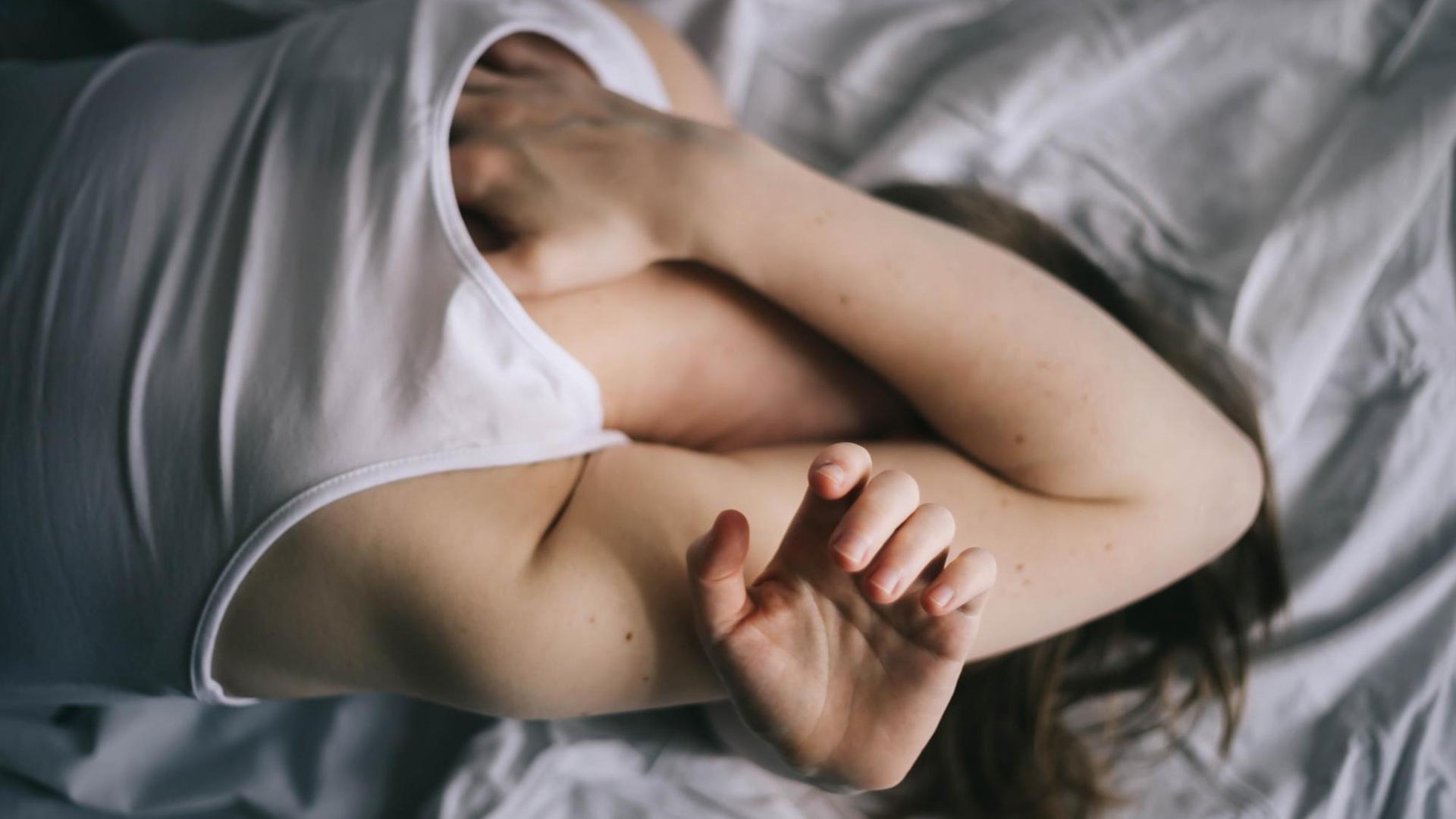 Eine Frau liegt im Bett und verbirgt das Gesicht unter ihren Armen. Eine Frau liegt im Bett und verbirgt das Gesicht unter ihren Armen.