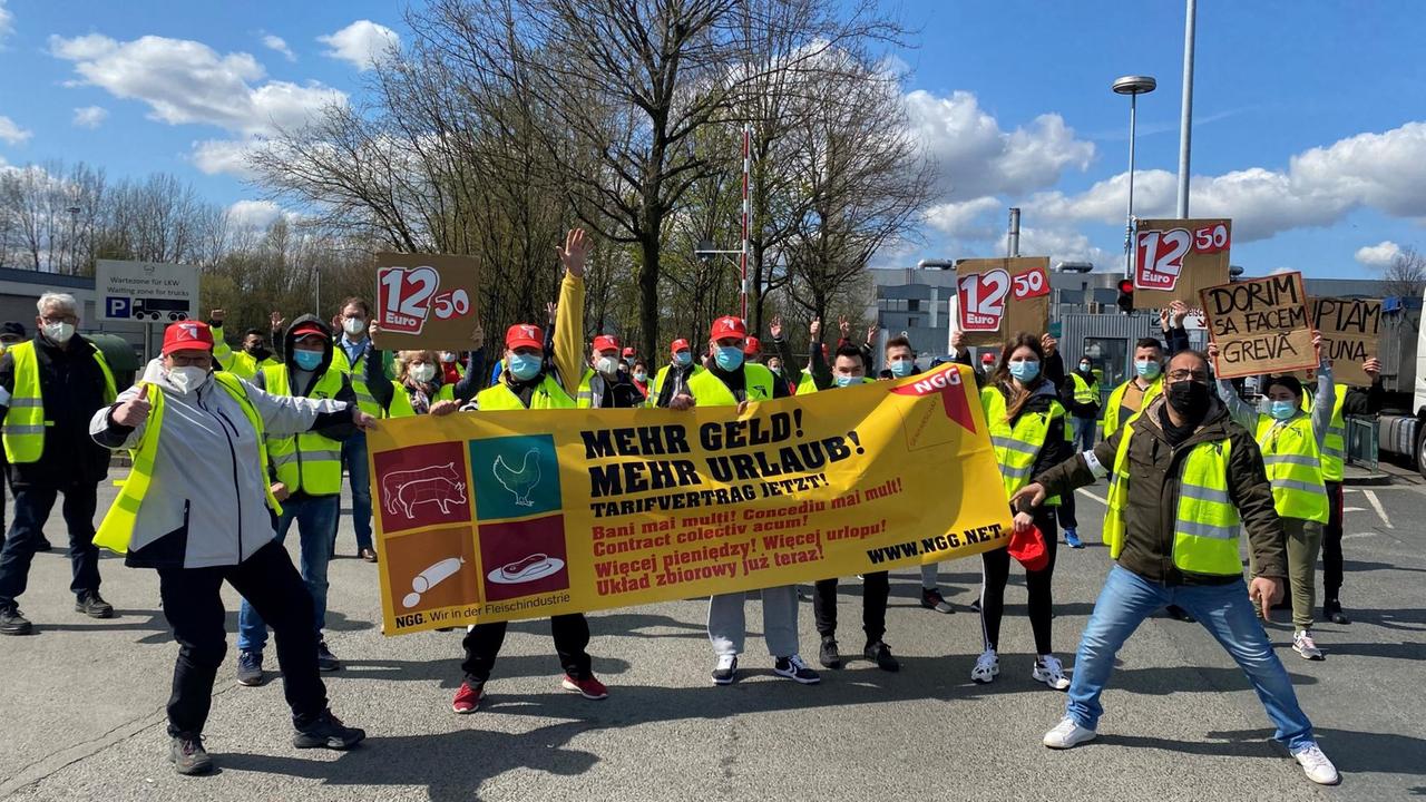 Arbeiter protestieren mit einem Banner, auf dem "Mehr Geld! Mehr Urlaub! Tarifvertrag jetzt!" seht, vor einem Werk. Arbeiter protestieren mit einem Banner, auf dem "Mehr Geld! Mehr Urlaub! Tarifvertrag jetzt!" seht, vor einem Werk.