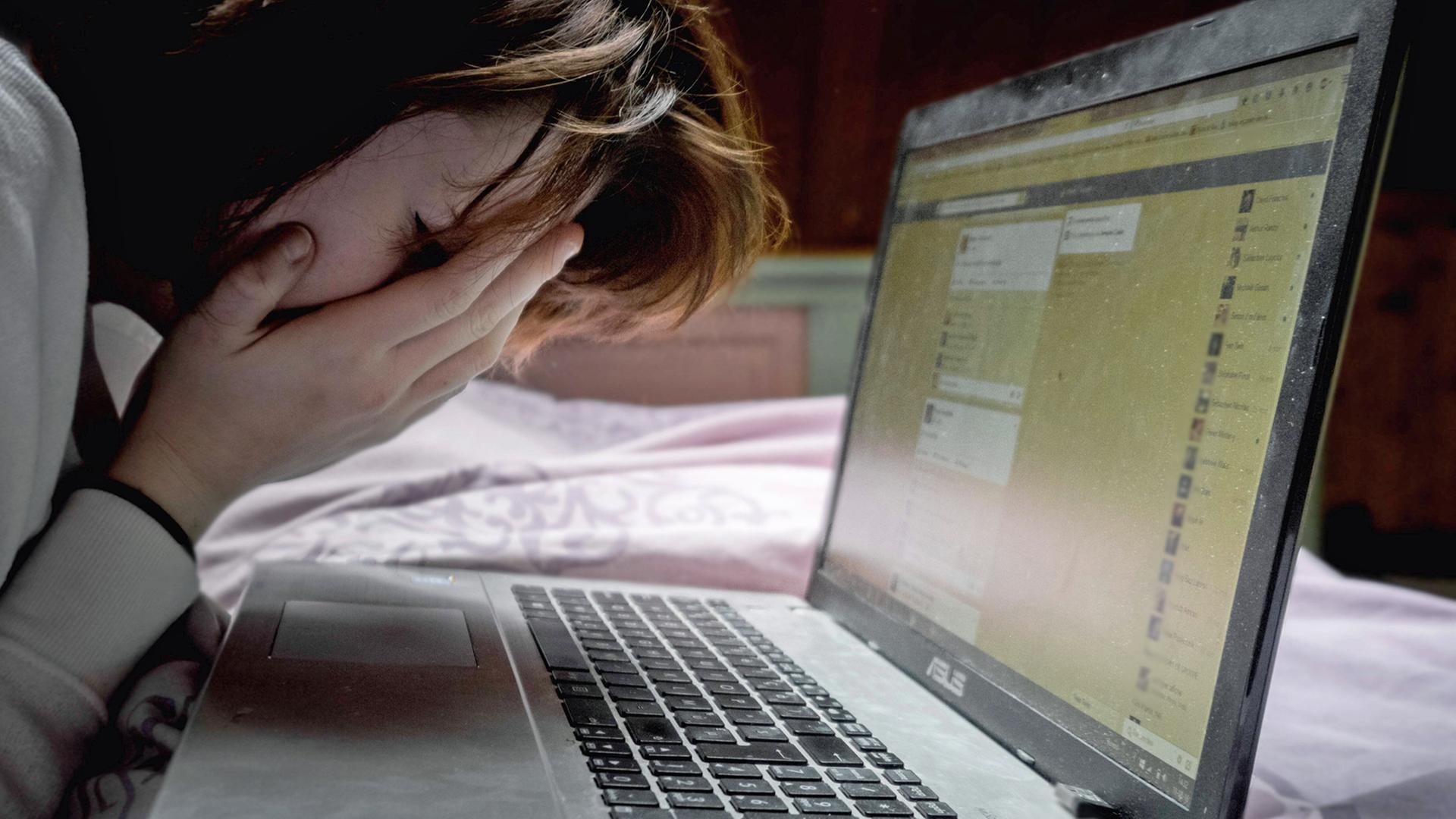 Eine Frau sitzt vor einem Laptop und schlägt angesichts von Hassbotschaften per Facebook die Hände vors Gesicht. Eine Frau sitzt vor einem Laptop und schlägt angesichts von Hassbotschaften per Facebook die Hände vors Gesicht.