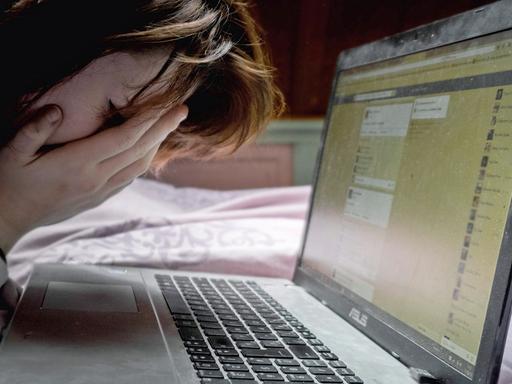 Eine Frau sitzt vor einem Laptop und schlägt angesichts von Hassbotschaften per Facebook die Hände vors Gesicht.