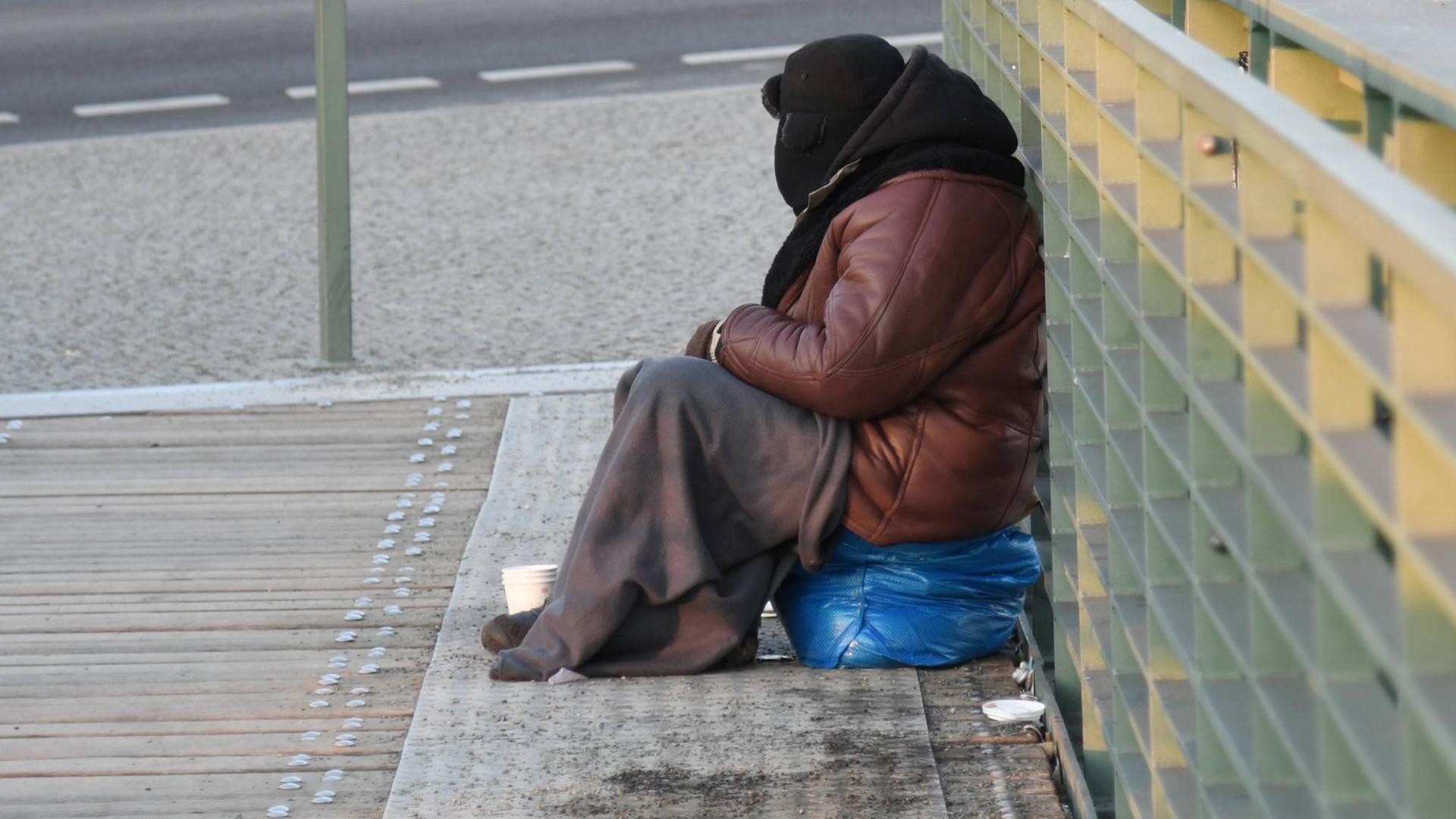 Ein Bettler, eingemummt in eine dicke Jacke,Pelzmuetze und Decke, sitzt bei bissiger Kaelte auf der Brücke vor dem Hauptbahnhof in Berlin. Ein Bettler, eingemummt in eine dicke Jacke,Pelzmuetze und Decke, sitzt bei bissiger Kaelte auf der Brücke vor dem Hauptbahnhof in Berlin.