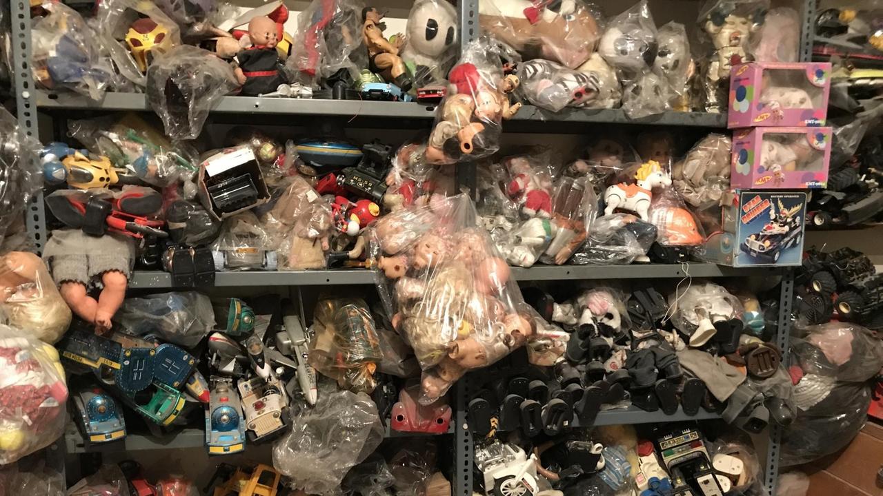 In mehreren Regalen übereinander hängt ein ganzer Wust von Kinderspielzeug heraus: Puppen, Autos etc. In mehreren Regalen übereinander hängt ein ganzer Wust von Kinderspielzeug heraus: Puppen, Autos etc.