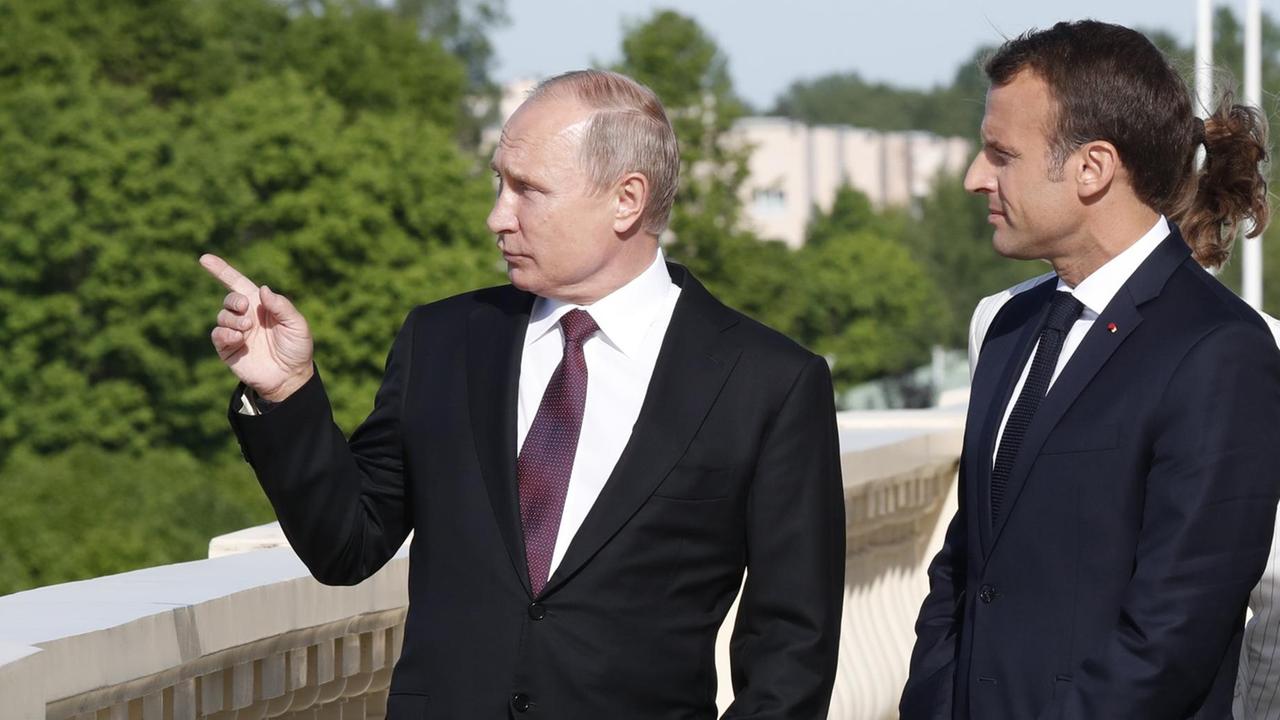 Putin weist Macron mit einer Geste vor dem Konstantinpalast auf etwas hin.