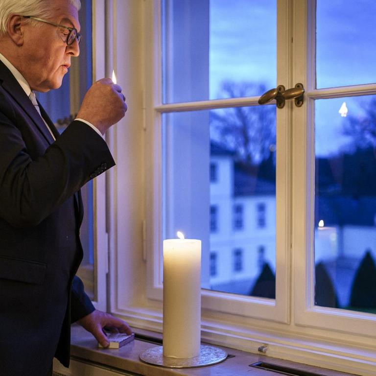 Bundespräsident Frank-Walter Steinmeier zündet eine Kerze vor einem Fenster an