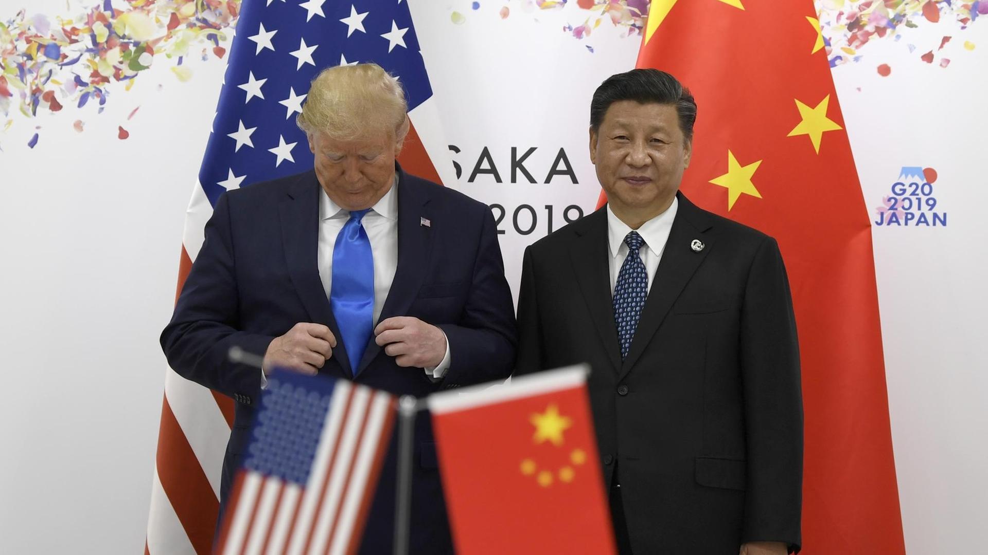 Donald Trump richtet seinen Anzug, während er auf dem G20-Gipfel mit Xi Jinping für ein Foto posiert. Donald Trump richtet seinen Anzug, während er auf dem G20-Gipfel mit Xi Jinping für ein Foto posiert.