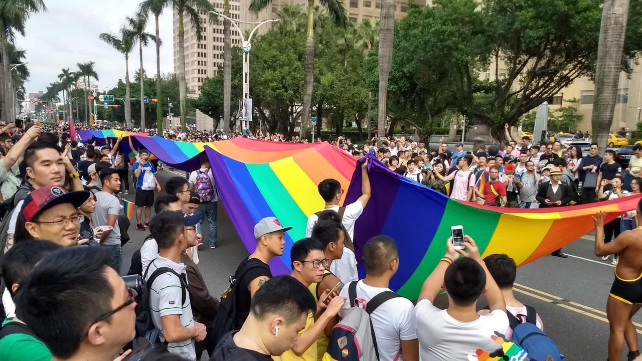 Vor allem männliche Teilnehmer der Gay Pride in Taipeh im Oktober 2017 tragen eine Regenbogenflagge durch die Straße. Vor allem männliche Teilnehmer der Gay Pride in Taipeh im Oktober 2017 tragen eine Regenbogenflagge durch die Straße.