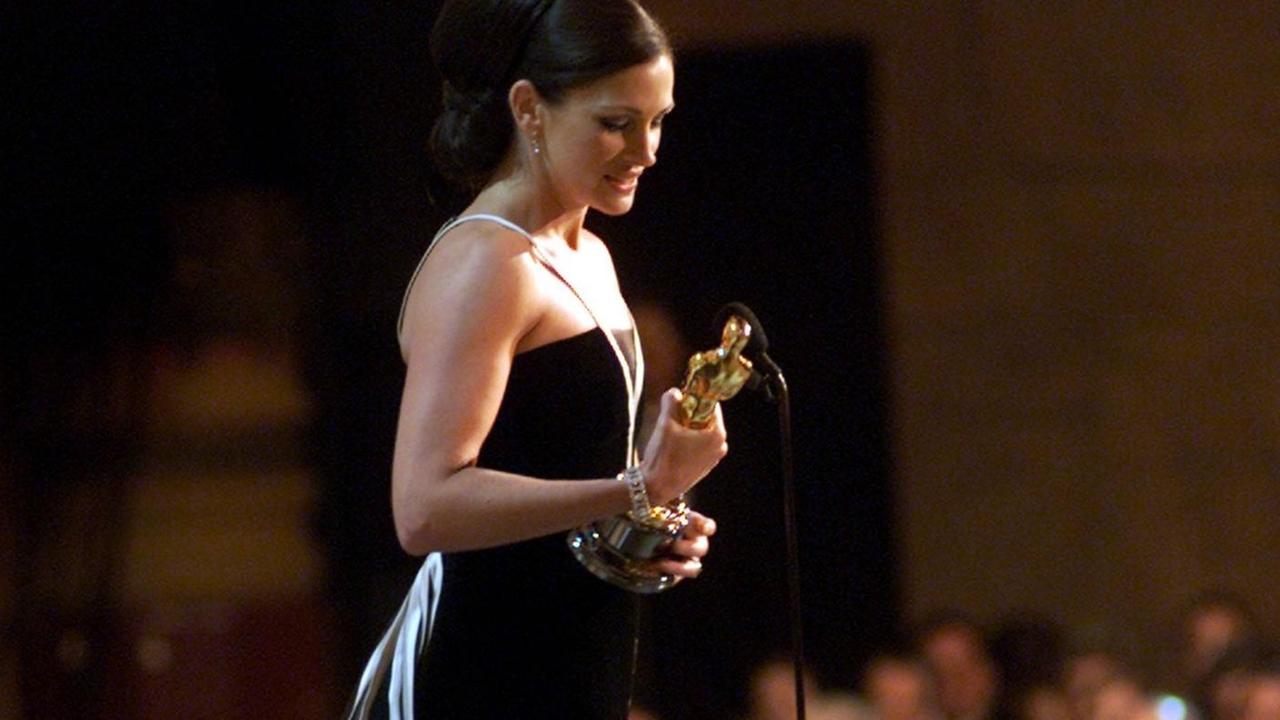 Julia Roberts steht in einem bodenlangen schwarzen Kleid auf der Bühne, betrachtet den Oscar in ihrer Hand und spricht zum Publikum.