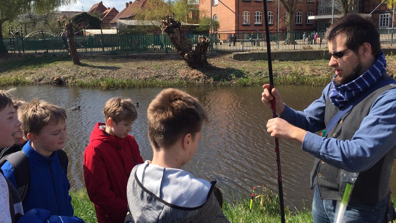 Auf der linken Seite steht Christoph Wittecke , Biologe und Projektleiter von "Angeln macht Schule", und erklärt den vor ihm stehenden vier Schülern eine Angel. Dahinter ist der Hagenower Mühlenteich zu sehen. Auf der linken Seite steht Christoph Wittecke , Biologe und Projektleiter von "Angeln macht Schule", und erklärt den vor ihm stehenden vier Schülern eine Angel. Dahinter ist der Hagenower Mühlenteich zu sehen.