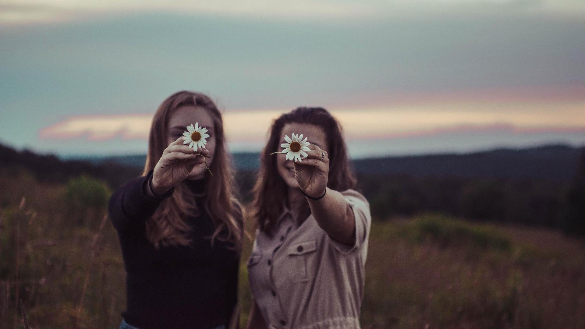 Zwei Frauen stehen nebeneinander und halten sich eine Blume vor das Gesicht. Zwei Frauen stehen nebeneinander und halten sich eine Blume vor das Gesicht.