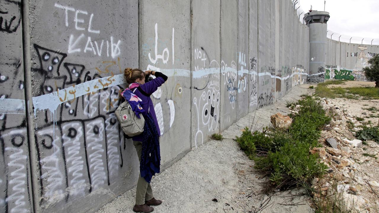 Eine junge Frau macht auf der palästinensischen Seite derr Sperrmauer zwischen Bethlehem, Westjordanland und Jerusalem ein Foto.