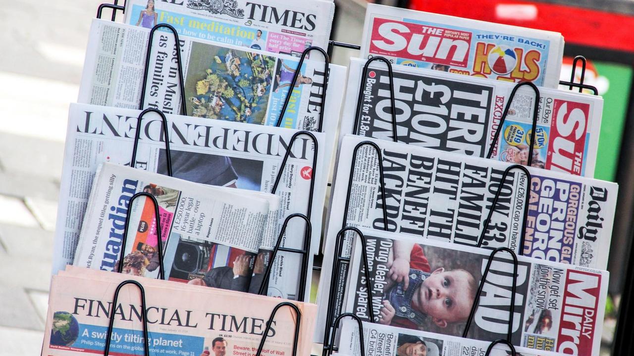 In dem Ständer klemmen unter anderem die Sun, der Daily Mirror, die Times und der Independent. Im Hintergrund unscharf ein Regal. In dem Ständer klemmen unter anderem die Sun, der Daily Mirror, die Times und der Independent. Im Hintergrund unscharf ein Regal.