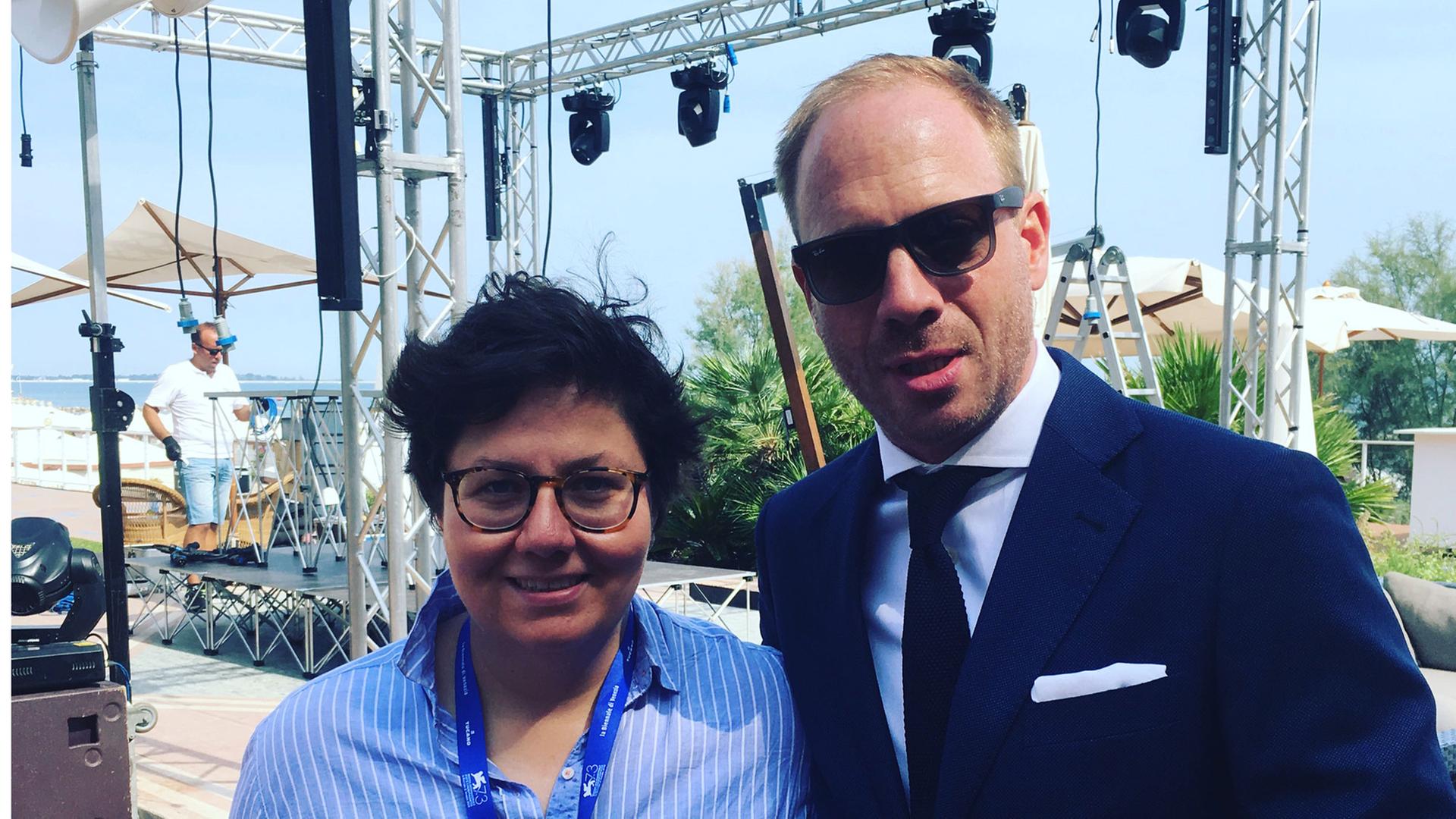 Schauspieler Johann von Bülow und die Autorin Anna Wollner bei den Filmfestspielen in Venedig 2016. Sie hat ihn einen Tag lang auf dem Lido begleitet. Beide lächeln fröhlich in die Kamera. Johann von Bülow trägt eine Sonnenbrille. Schauspieler Johann von Bülow und die Autorin Anna Wollner bei den Filmfestspielen in Venedig 2016. Sie hat ihn einen Tag lang auf dem Lido begleitet. Beide lächeln fröhlich in die Kamera. Johann von Bülow trägt eine Sonnenbrille.