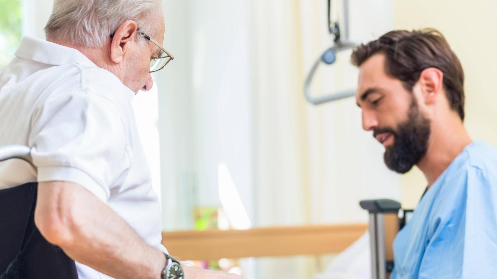 Ein Krankenpfleger hilft einem älteren Mann vom Bett in den Rollstuhl Ein Krankenpfleger hilft einem älteren Mann vom Bett in den Rollstuhl