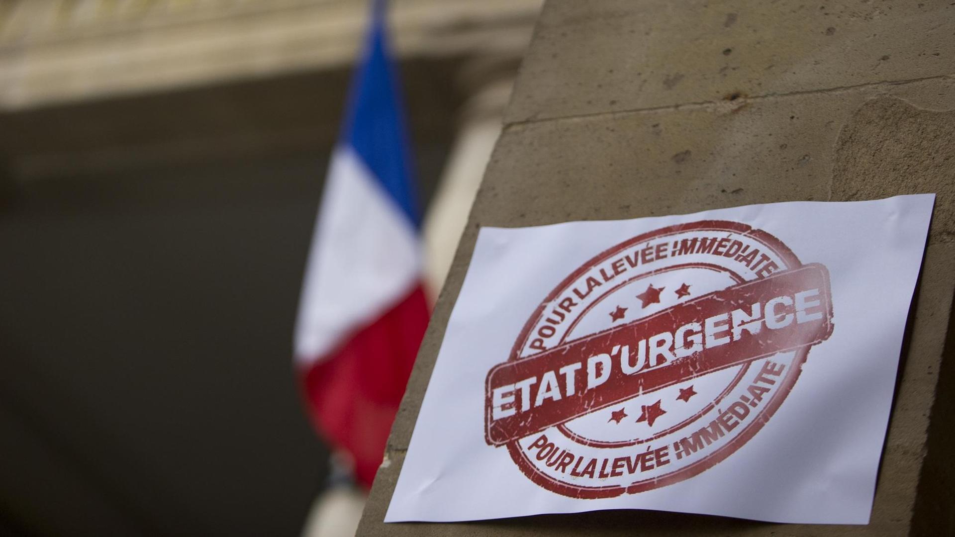 Protestplakat gegen den verhängten Ausnahmezustand in Frankreich klebt am Eingang des Französischen Verfassungsrates. Im Hintergrund ist die französische Flagge zu sehen.