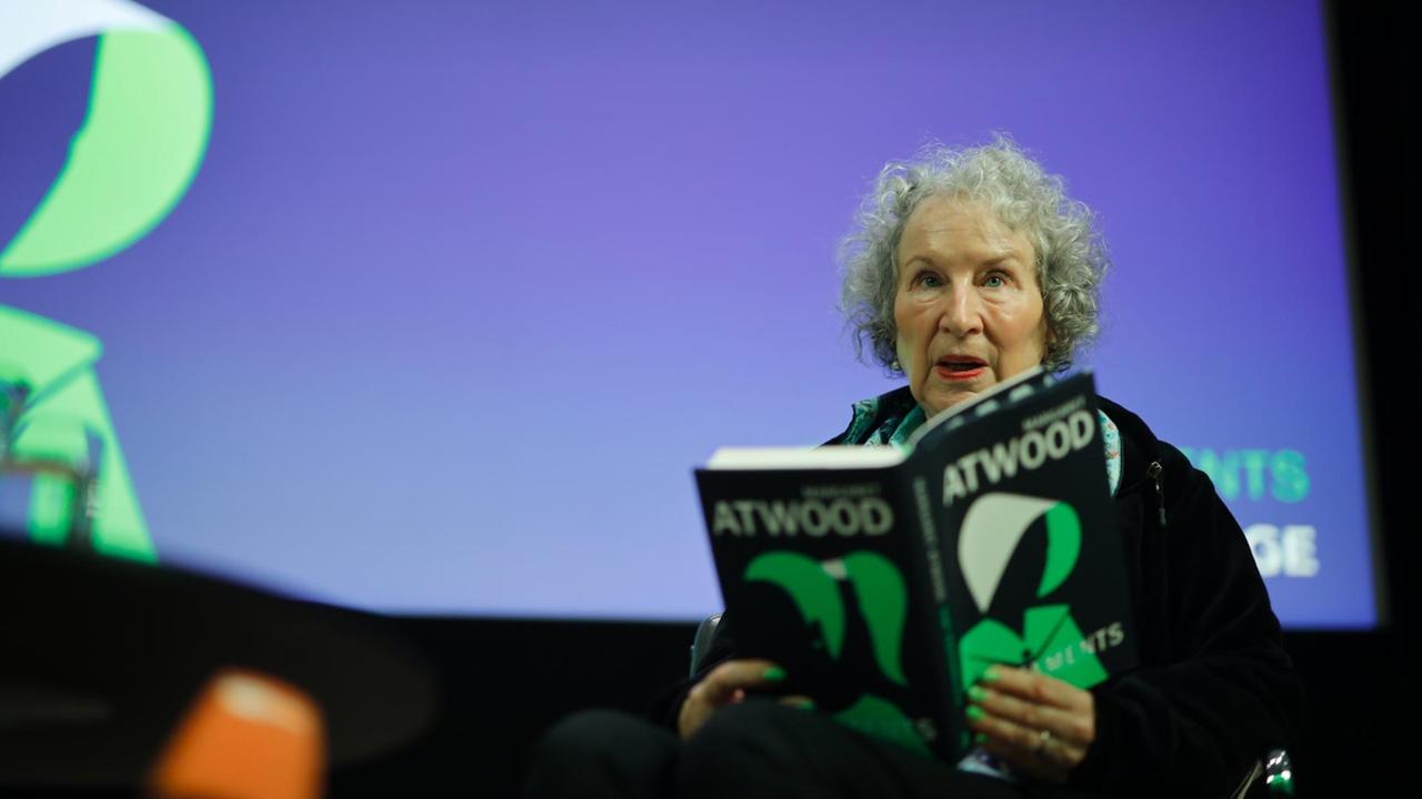 Margaret Atwood sitzt mit einem Buch in der Hand auf einem Podium.