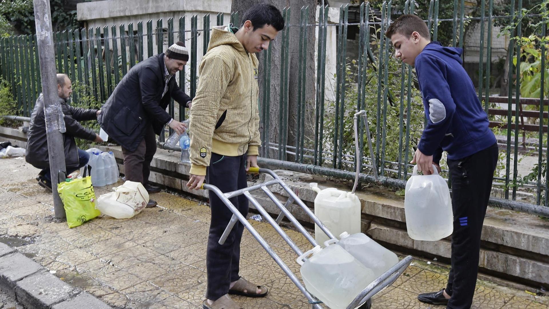 Vier Syrer befüllen ihre Wasserkanister an einem öffentlichen Brunnen der Hauptstadt Damaskus.