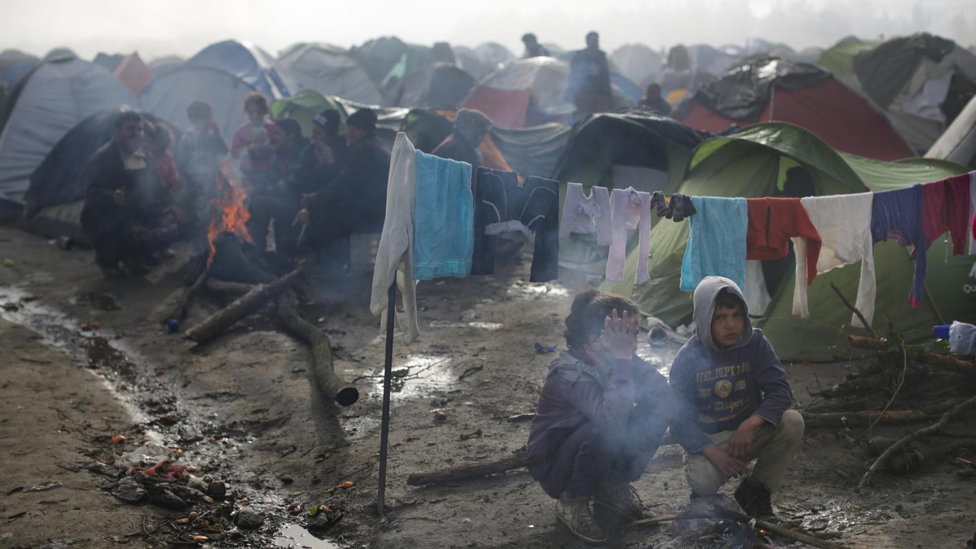 Zwei Flüchtlingskinder sitzen im Flüchtlingslager in Idomeni an der Grenze zwischen Griechenland und Mazedonien an einer Feuerstelle. Starker Regen und Temperaturen um die fünf Grad haben die Situation der Flüchtlinge noch erschwert. Zwei Flüchtlingskinder sitzen im Flüchtlingslager in Idomeni an der Grenze zwischen Griechenland und Mazedonien an einer Feuerstelle. Starker Regen und Temperaturen um die fünf Grad haben die Situation der Flüchtlinge noch erschwert.