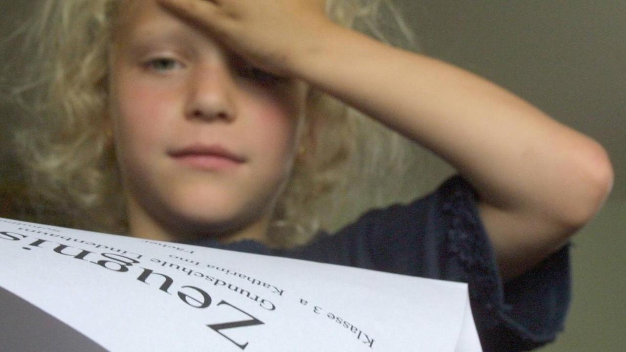 Ein Mädchen begutachtet ihr Zeugnis und hält sich die Hand an die Stirn. Ein Mädchen begutachtet ihr Zeugnis und hält sich die Hand an die Stirn.