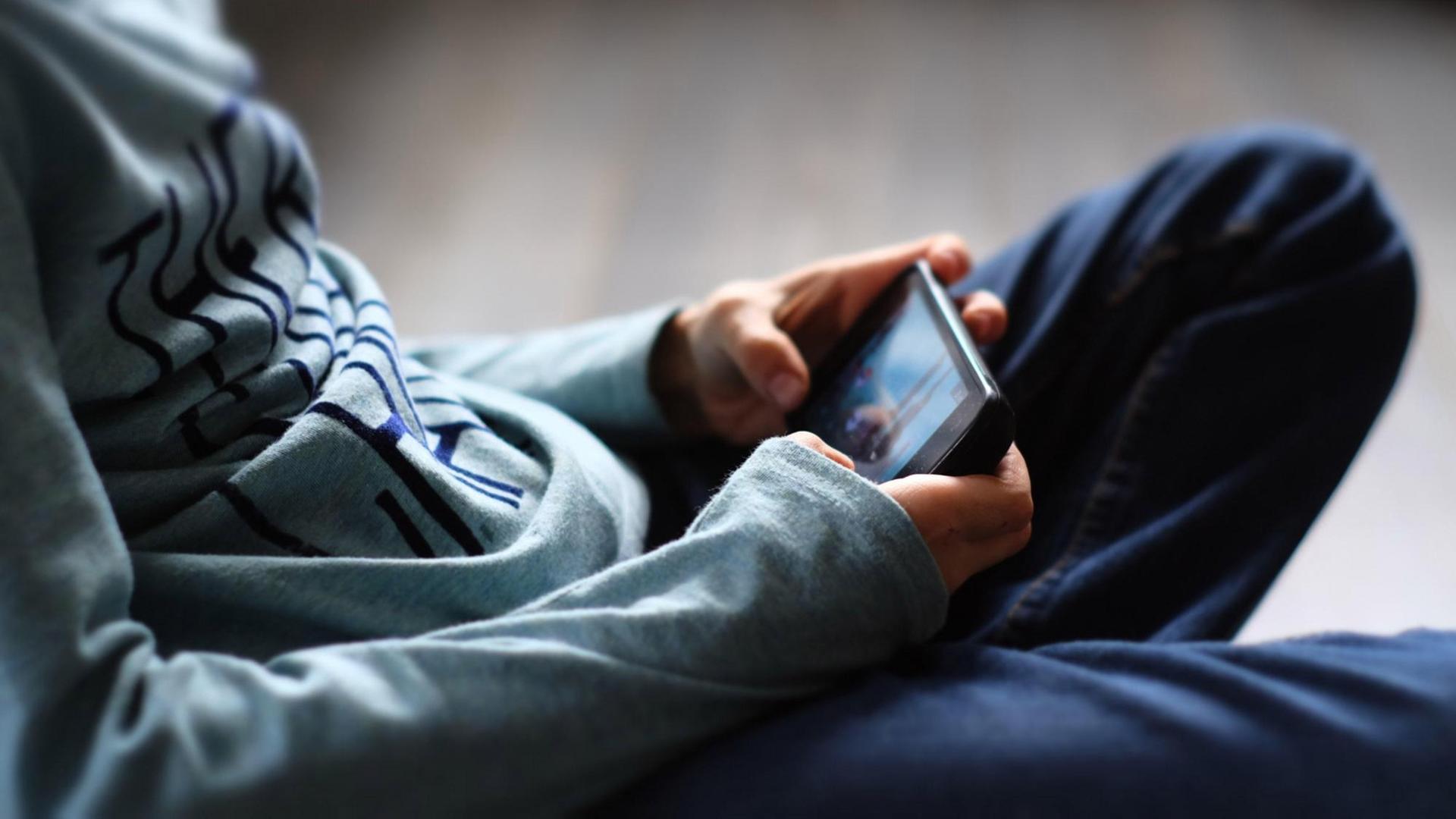 Oberjörper eines Jungen, der sitzend mit dem Handy spielt (Symbolbild)