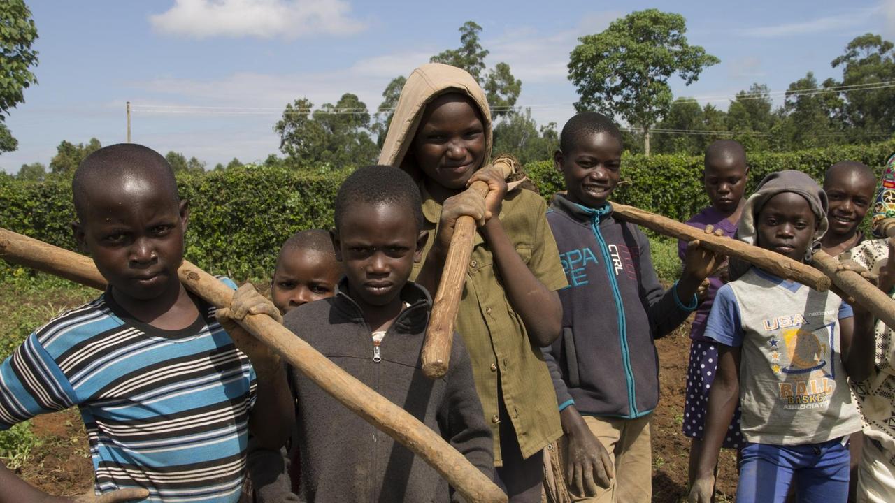 Eine Gruppe afrikanischer Jungen hat Gartengeräte geschultert.