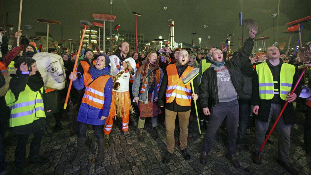 Anti-Pegida-Demonstranten in Dresden mit Warnwesten und Besen. Dresdner Künstler fegten am 5. Januar 2015 mit einem Kehraus - einem Neujahrsputz - den Platz der Pegida-Kundgebung symbolisch sauber. Anti-Pegida-Demonstranten in Dresden mit Warnwesten und Besen. Dresdner Künstler fegten am 5. Januar 2015 mit einem Kehraus - einem Neujahrsputz - den Platz der Pegida-Kundgebung symbolisch sauber.