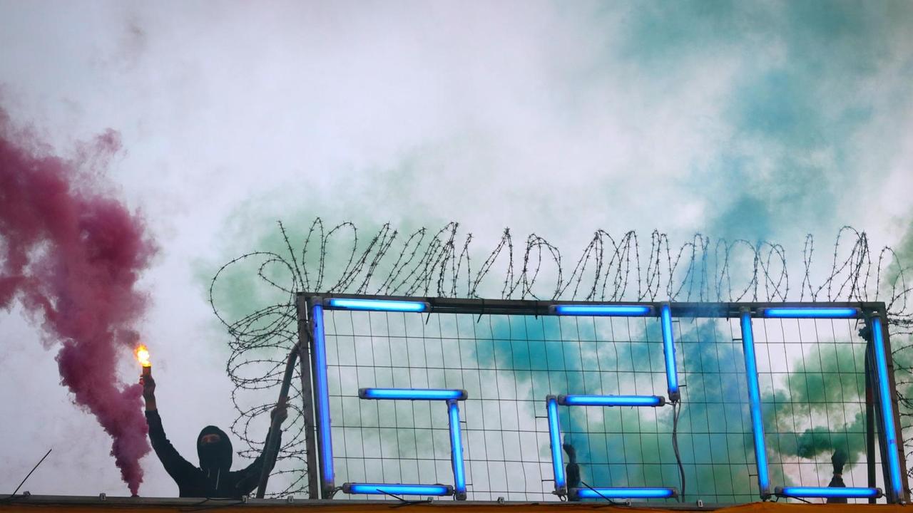 Ein Aktivist mit Bengalos steht am 05.07.2017 in Hamburg auf dem Dach der Roten Flora neben einem G20-Schriftzug, während eine Demonstration gegen den bevorstehenden G20-Gipfel an dem Kulturzentrum vorbeizieht. Am 06. und 07. Juli kommen in der Hansestadt die Regierungschefs der führenden Industrienationen zum G20-Gipfel zusammen. 