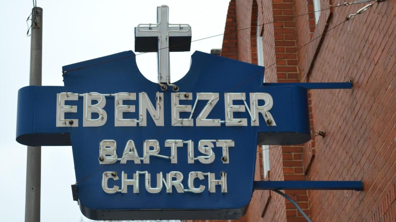 An einer Hauswand hängt eine blaue Leuchtreklame der Ebenezer Baptist Church