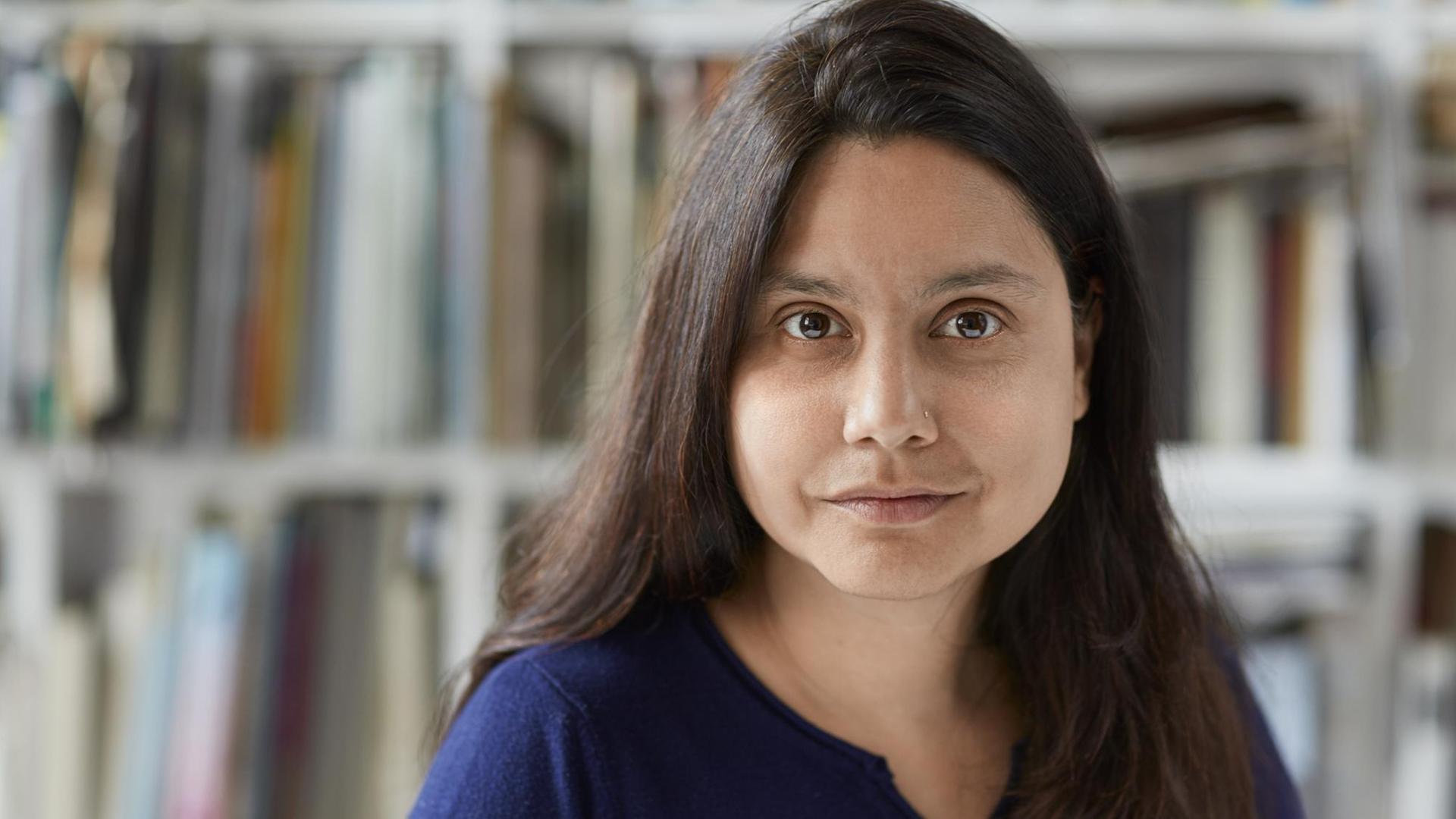 Die Autorin Mithu Sanyal blickt vor einem Bücherregal in die Kamera. Die Autorin Mithu Sanyal blickt vor einem Bücherregal in die Kamera.