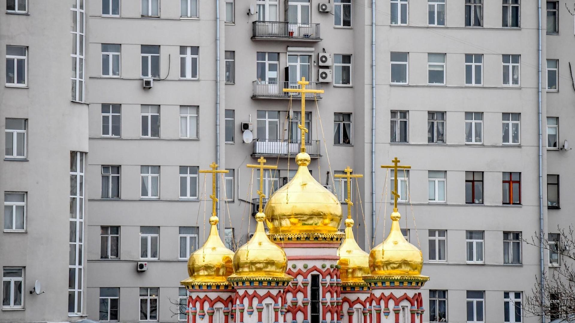 Eine orthodoxe Kirche mit goldenen Zwiebeltürmen steht vor einem grauen Wohnblock