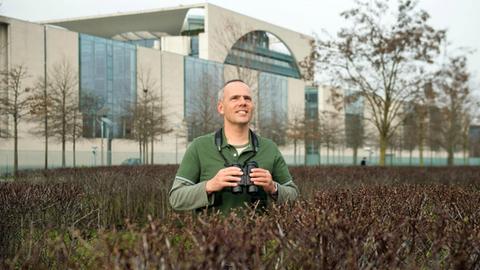 Der Pressereferent und ehemalige Wildtierbeauftragter der Senatsverwaltung für Stadtentwicklung und Umwelt, Derk Ehlert, steht im Tiergarten in Berlin, im Hintergrund das Bundeskanzleramt.